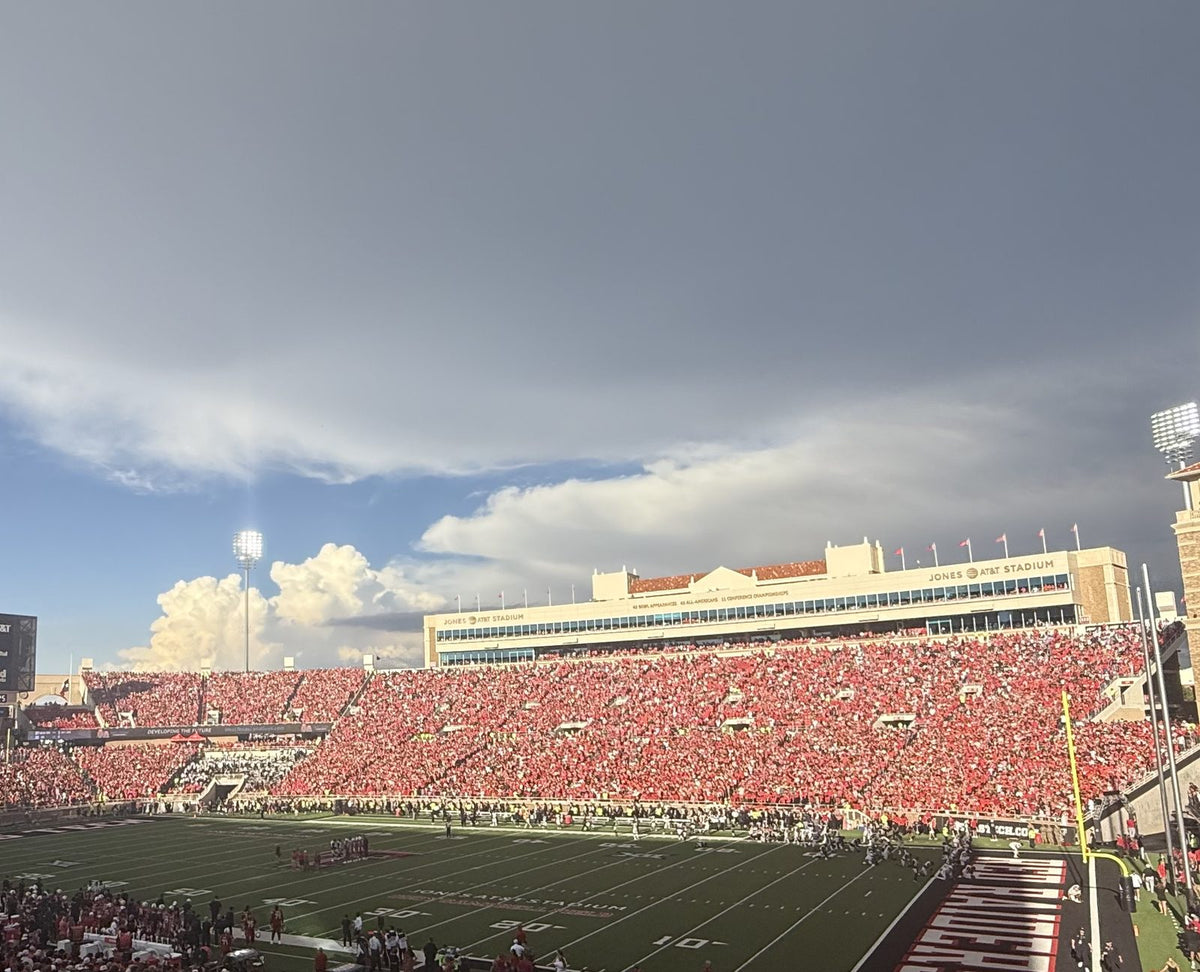 Packed red stands under a dramatic West Texas sky